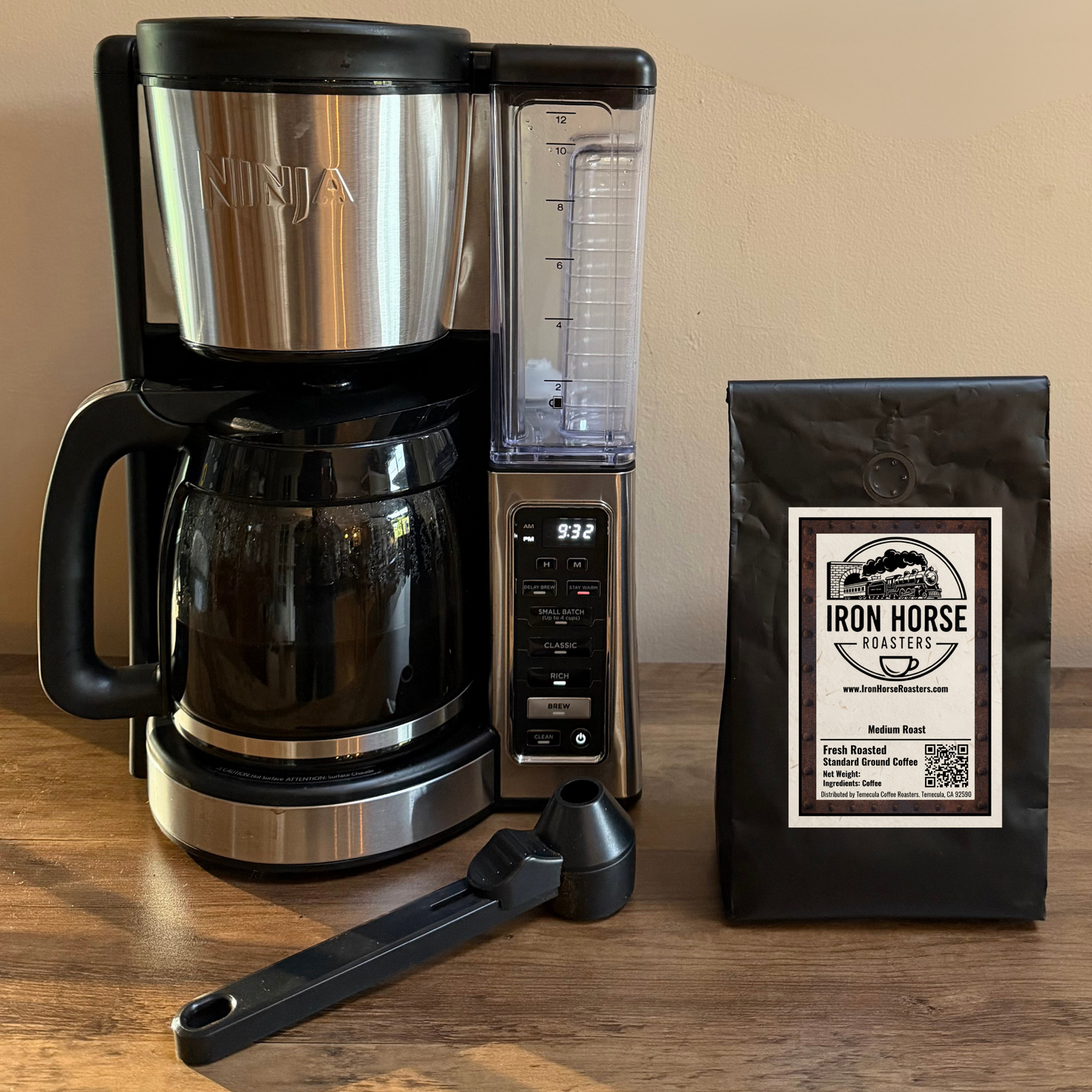 Black coffee bag and white mug with 'Iron Horse Roasters' logo on a wooden surface with coffee beans and a blurred background at coffee shop